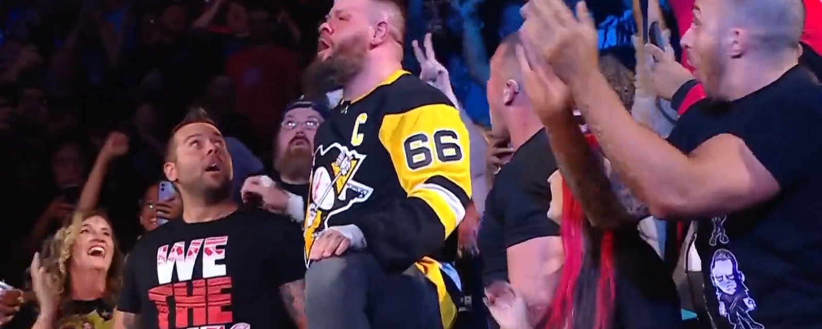 Kevin Owens jumps off railing wearing Mario Lemieux jersey.